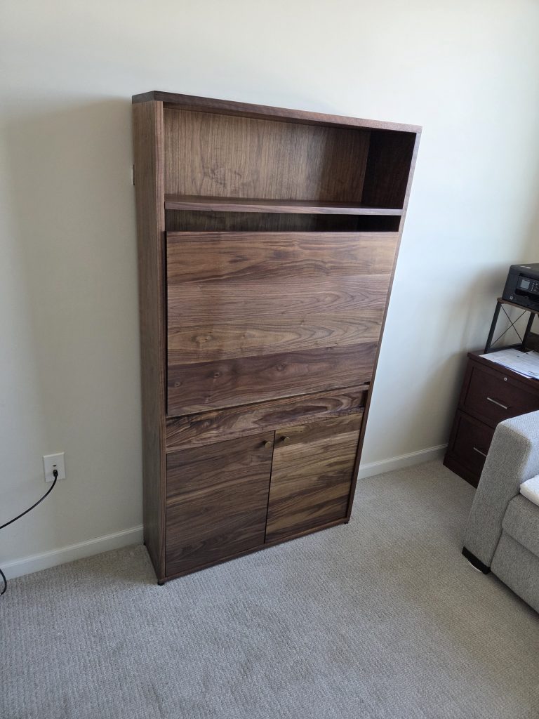 Tall walnut-toned wooden storage cabinet with an open top shelf and closed drawer/door compartments in a carpeted room corner