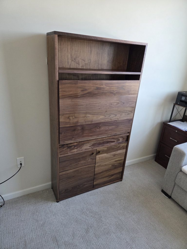 Tall wooden dresser with an open upper compartment and multiple drawers, placed against a pale wall in a carpeted room.