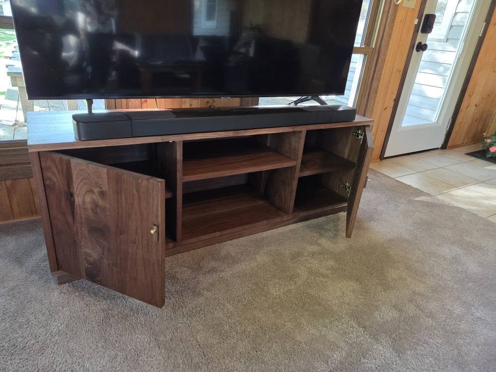 Wooden media console with a large flat-screen TV on top and open shelves, two cupboard doors swung open.