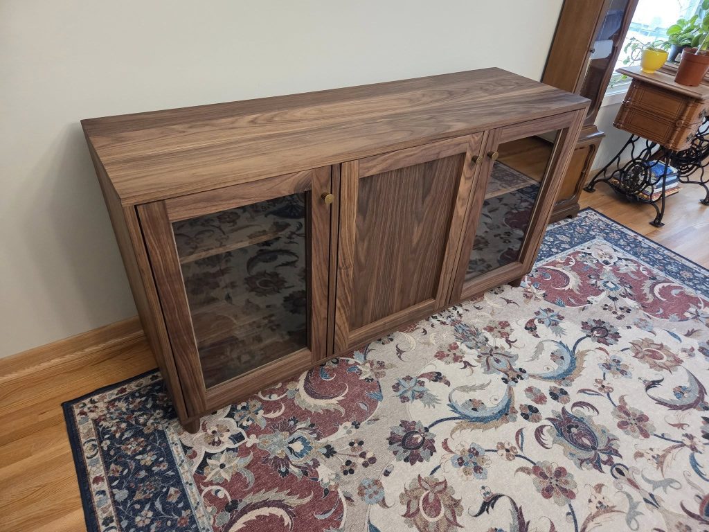 Oak-toned wooden sideboard with glass-front cabinets in a living room on a patterned rug